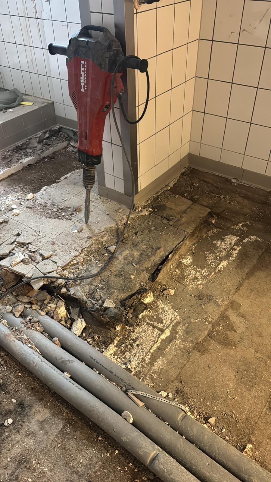 Bodenabbruch mit Abbruchhammer neben freigelegten Leitungen in einer Gewerbeküche