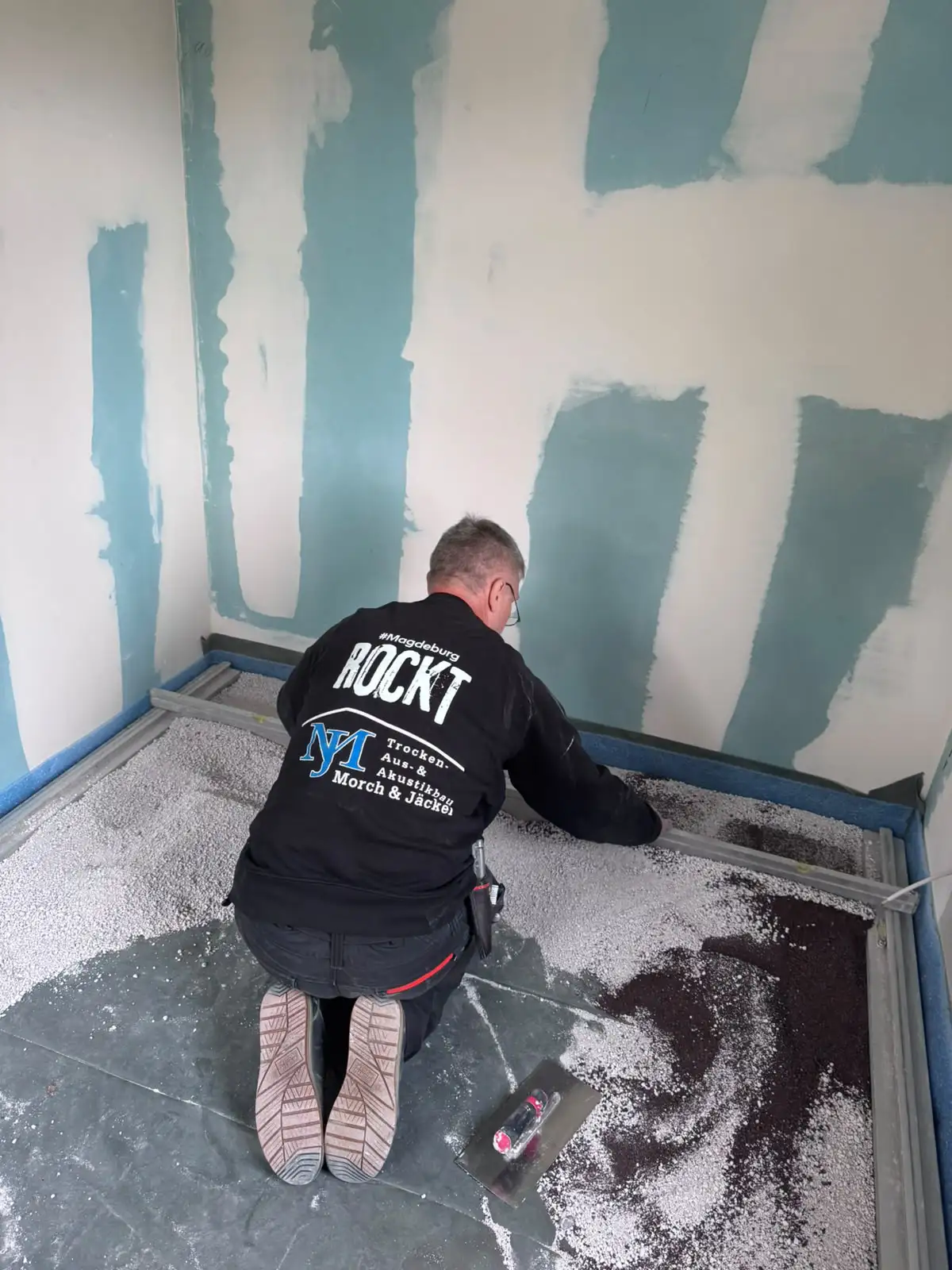 Handwerker kniet auf dem Boden und verteilt die Ausgleichsschüttung entlang der Alu-Schiene in Niederndodeleben